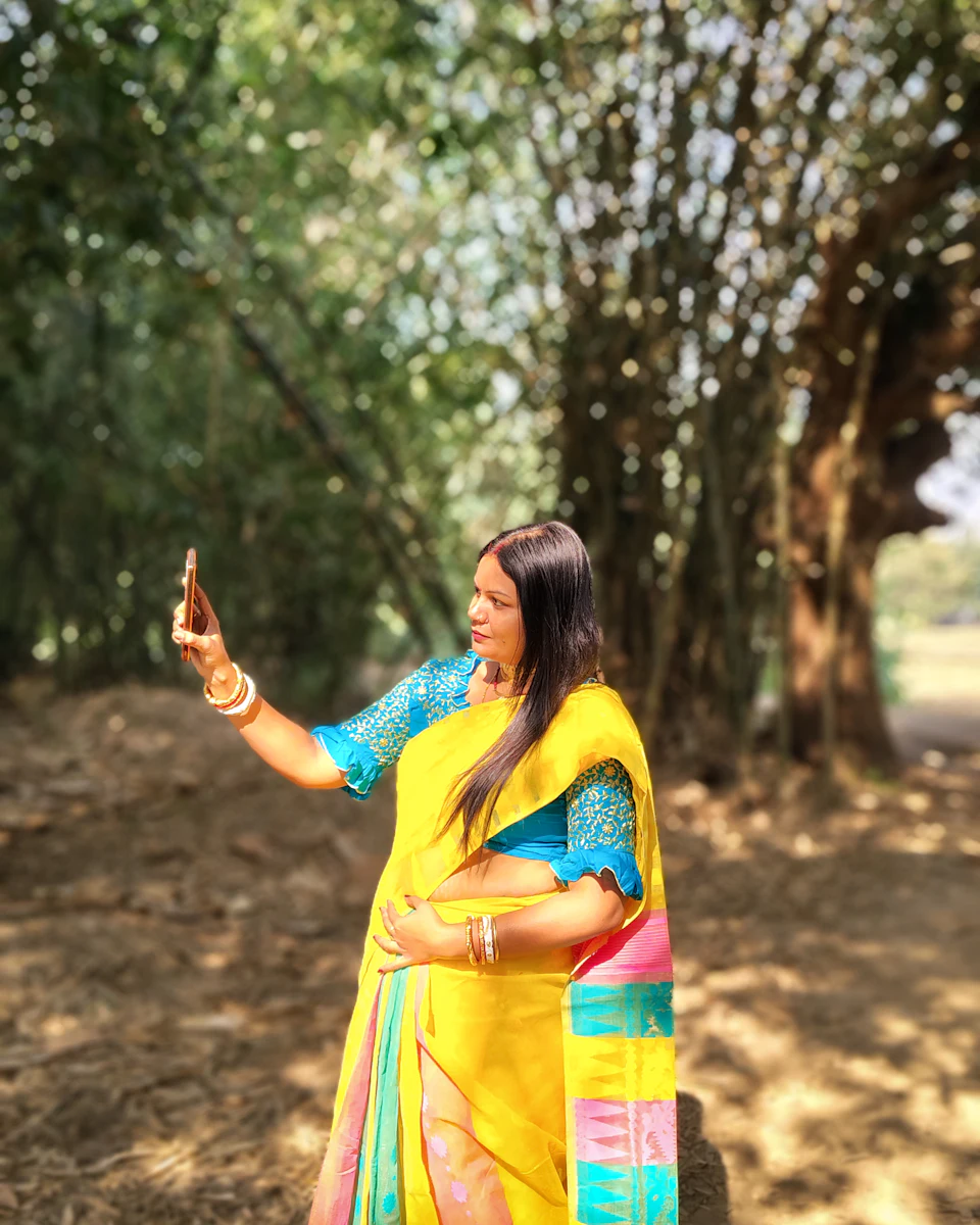 A woman in a yellow sari filming herself on her phone outdoors